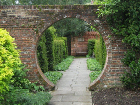 Snitsig manport i tegelmur i harmonisk trädgård – trädgårdsdesign av trädgårdsarkitekt/landskapsingenjör i samspel med naturen, med hållbara material, växtkomposition och rumslighet.