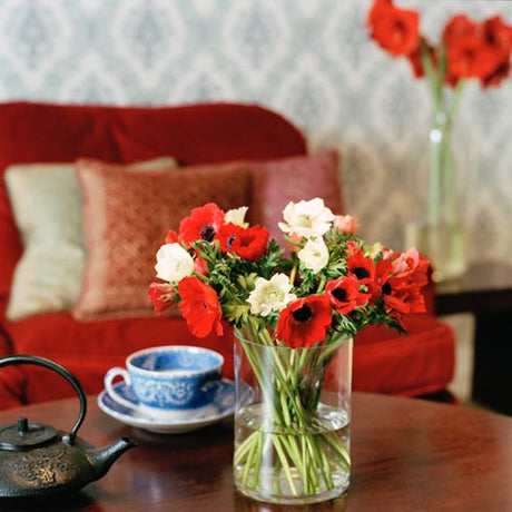 Julbukett med röda och vita snittblommor – amaryllis, rosor, liljor, ranunkel och hyacint – omgiven av eukalyptus, järnek och murgröna, dekorerad med kvistar, kanel och stjärnanis.