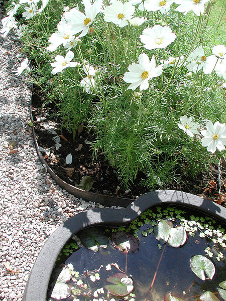 Stålkant mot grusad yta som rabattkant mellan gräsmatta och rabatt – hållbart, barnsäkert alternativ; återbruk av hängrännor/stuprännor i metall minskar ogräs och förenklar gräsklippning.